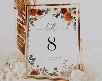 May include: A gold framed table number 8 card with floral accents. The card features the word "table" in script, the number 8 in a bold font, and the names Cecilia & Harrison with the date July 26, 20XX.
