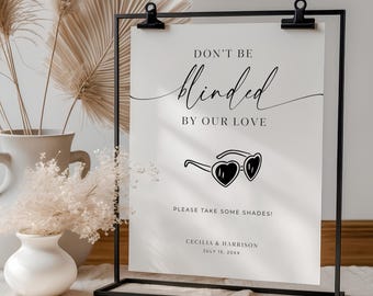 May include: A black metal sign holder displays a white sign with the text "DON'T BE blinded BY OUR LOVE." Below is a graphic of heart-shaped sunglasses. The sign also includes the names Cecilia & Harrison and the date July 15, 20XX.