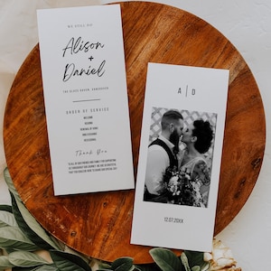 Może przedstawiać: Dwa białe programy ślubne z czarnym tekstem na drewnianej powierzchni. Jeden program głosi "Alison + Daniel" i "The Glass Haven, Vancouver". Drugi program ma zdjęcie całującej się pary i inicjały "A | D."