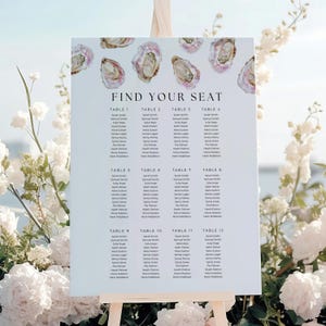 May include: A white seating plan featuring the text "FIND YOUR SEAT" and oyster illustrations. The plan lists names under the headings "TABLE 1" to "TABLE 12". It's displayed on a wooden easel, surrounded by white flowers, ideal for a wedding.