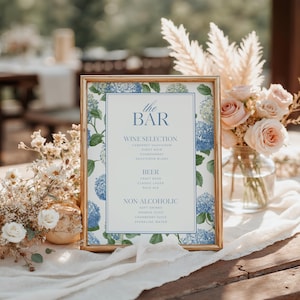 Elegant blue hydrangea wedding bar menu sign featuring soft blue hydrangea florals and greenery surrounding a classic framed drink menu layout. Floral bar menu sign designed for wedding receptions, garden weddings, and elegant outdoor celebrations. Editable and printable Canva template perfect for hydrangea themed weddings, blue floral wedding decor, signature drink menus, and sophisticated wedding bar signage.