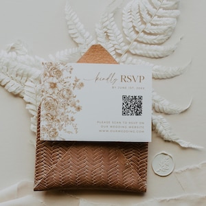 May include: A white RSVP card with floral illustrations and the text "kindly RSVP". The card includes a QR code and website address. It rests on a textured brown envelope, with a white floral wax seal.