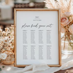 May include: A framed wedding seating chart with a gold-colored frame. The chart features the text "S&C" and "July 15, 20XX" at the top, followed by "please find your seat." Names are listed under table numbers.