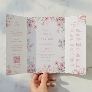 May include: A tri-fold wedding invitation with pink, blue, and white floral decorations. The invitation includes details such as the venue, attire, and RSVP information. The invitation also includes the wedding day schedule.
