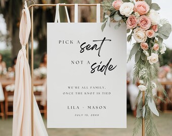 May include: White wedding sign with black calligraphy text that reads "Pick a seat, not a side. We're all family, once the knot is tied. Lila - Mason. July 15, 20XX".