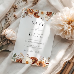 May include: A wedding invitation with the text "SAVE THE DATE" in black script. The invitation is decorated with floral elements in shades of brown, white, and orange. The invitation includes the names Cecilia & Harrison and the date July 26, 20XX.