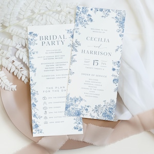 May include: Two wedding programs with blue floral designs. The programs include the text "Bridal Party" and "Cecilia and Harrison" with the date. The programs are on a pink plate with a white fern and a pink ribbon.