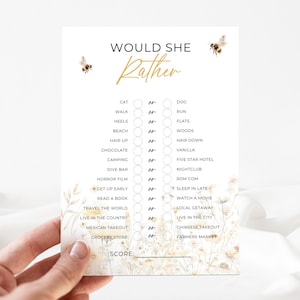 May include: A white card with the text "WOULD SHE Rather" in gold script, featuring a game with choices like "Cat" or "Dog". Floral and bee illustrations decorate the card. The card is held by a hand.