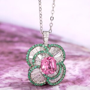 Peut inclure: Un collier en argent délicat avec un pendentif en pierre précieuse rose entouré de petites pierres précieuses vertes et blanches. Le pendentif est en forme de fleur à quatre pétales.