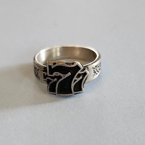 May include: A silver ring with a black number seven on the front. The band of the ring is decorated with a floral design.