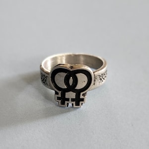 Può includere: Un anello d'argento con un design a doppio simbolo femminile nero.