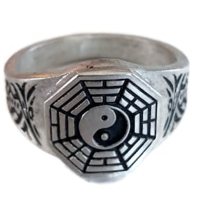 Puede incluir: Un anillo de plata con un símbolo yin yang blanco y negro dentro de un octógono plateado. El anillo está decorado con intrincados diseños plateados.