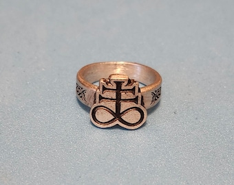 May include: A silver ring with a black engraved symbol of a cross with an infinity symbol at the bottom. The ring band is also engraved with a design.
