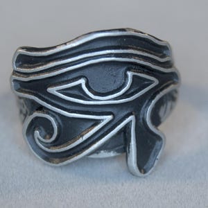 Puede incluir: Un anillo de plata con un diseño de ojo de Horus negro.