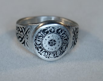 May include: A silver ring with a circular design featuring zodiac symbols and a pentagram in the center.