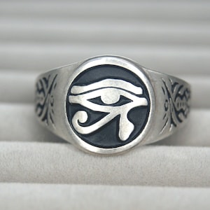 Puede incluir: Un anillo de plata con una incrustación de esmalte negro que representa el Ojo de Horus.