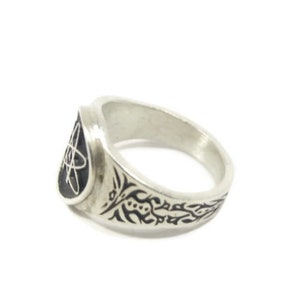 May include: A silver ring featuring a black atom symbol on the front and a black floral design on the band.