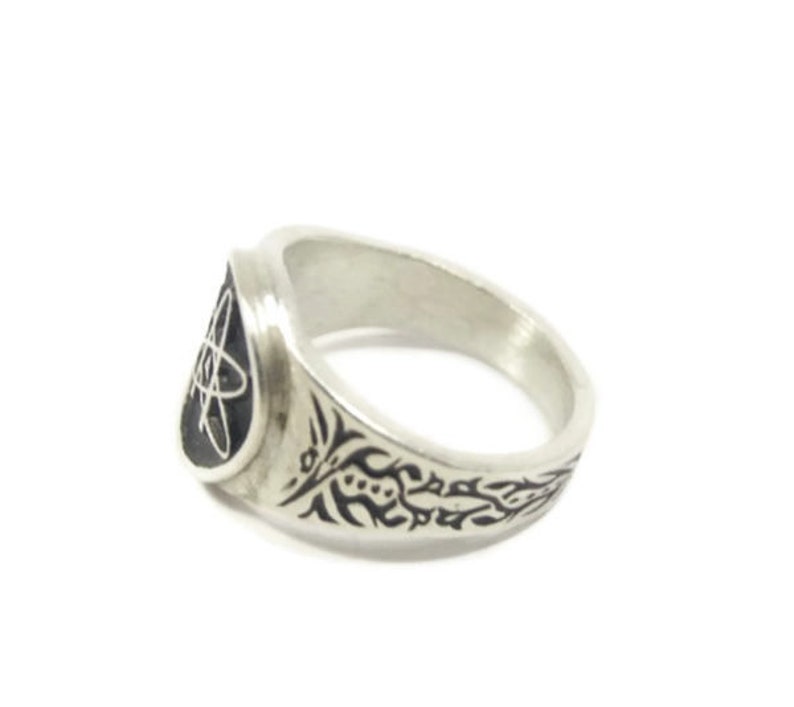 May include: A silver ring featuring a black atom symbol on the front and a black floral design on the band.