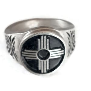 May include: A silver ring with a black and silver inlay of the Zia symbol, a traditional Native American design.