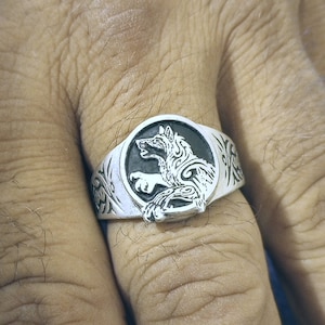 May include: A silver ring with a black wolf design. The wolf is in a circular setting with intricate details around the edges.