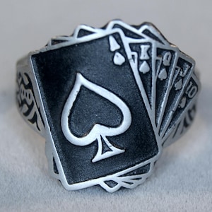 Puede incluir: Un anillo de plata con un diseño de cartas de juego, con el as de picas en el centro.