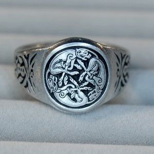 Puede incluir: Un anillo de plata con un diseño circular que presenta un nudo celta de cuatro animales entrelazados. El anillo tiene un acabado liso y pulido.