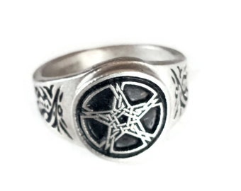 Puede incluir: Un anillo de plata con un diseño circular negro que presenta una estrella de cinco puntas con detalles intrincados. La banda del anillo está decorada con un patrón floral.