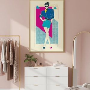 May include: A framed art print featuring a stylized illustration of a person in a blue jacket and teal skirt. The artwork has a retro aesthetic with geometric shapes in pink, teal, and yellow. The print is displayed in a room with a white dresser and gold accents.