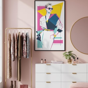 May include: A framed art print of a stylish person in sunglasses, wearing a polka dot top and white pants. A gold clothing rack with dresses and a white dresser with gold accents are also in the room. A pink ottoman and a round mirror complete the scene.