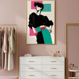 May include: A framed art print featuring a stylized illustration of a person in a black top, teal skirt, and a pink and teal background. The artwork is displayed above a white dresser with gold hardware.