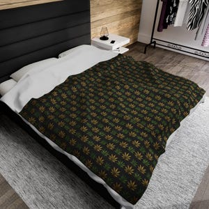 May include: A black and white patterned throw blanket with a repeating design of green and gold marijuana leaves.