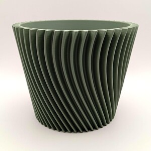 Könnte beinhalten: Ein salbeigrüner, 3D-gedruckter Pflanztopf mit einem einzigartigen, wirbelnden Rippendesign. Der Topf hat einen breiten, geriffelten Rand und eine konische Form. Die vertikalen Linien erzeugen eine strukturierte, auffällige Ästhetik. Etwa 15 cm hoch.