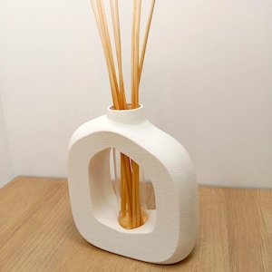 Può includere: Diffusore in ceramica bianca, strutturata, con un'originale apertura ovale. Contiene un recipiente di vetro trasparente pieno di bastoncini di canna marrone chiaro. I bastoncini diffondono la fragranza, creando un elemento decorativo.