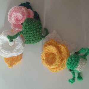 Peut inclure: Trois ornements en forme de fleur crochetés avec des grenouilles en crochet vert attachées. Les fleurs sont blanches, roses et jaunes.