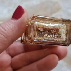 May include: A clear glass bottle with a gold label that reads "Guerlain Paris" and "15 ml guerlain-paris 6900 MK0994C".
