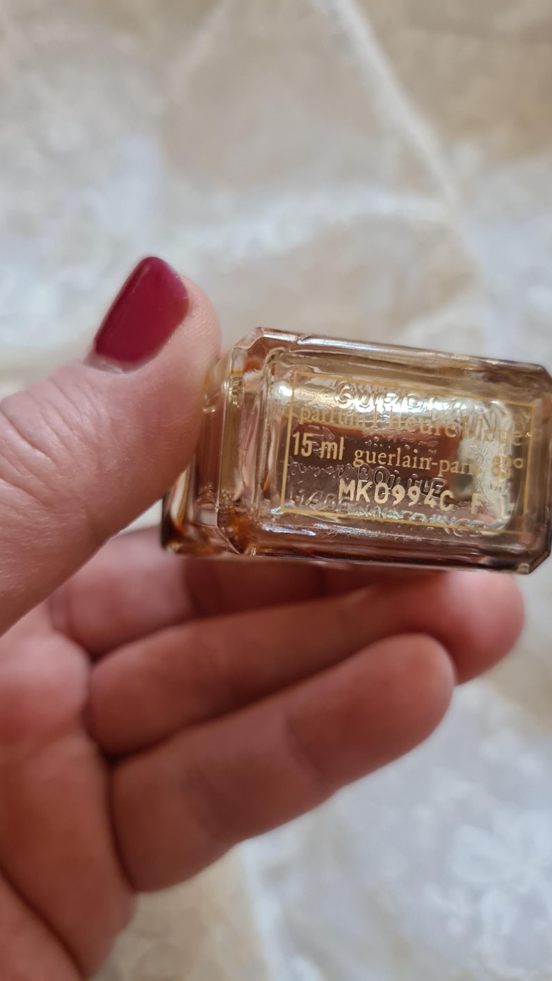 May include: A clear glass bottle with a gold label that reads "Guerlain Paris" and "15 ml guerlain-paris 6900 MK0994C".