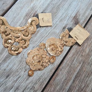 May include: Two gold sequined fabric patches, one shaped like a collar and the other shaped like a flower, on a wooden surface.