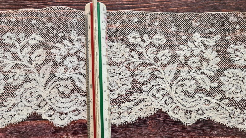 Puede incluir: Ribete de encaje marfil con dise&ntilde;o floral, con hojas y flores detalladas. Una regla muestra el ancho del encaje. El encaje tiene un borde festoneado y un tejido abierto y delicado, adecuado para proyectos de manualidades. El encaje mide unos 10 cm de ancho.