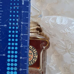 May include: A small glass bottle with a brown liquid inside. The bottle has a gold-colored label with the text "Irish Mist" and a shamrock design. The bottle is about 5 cm tall.