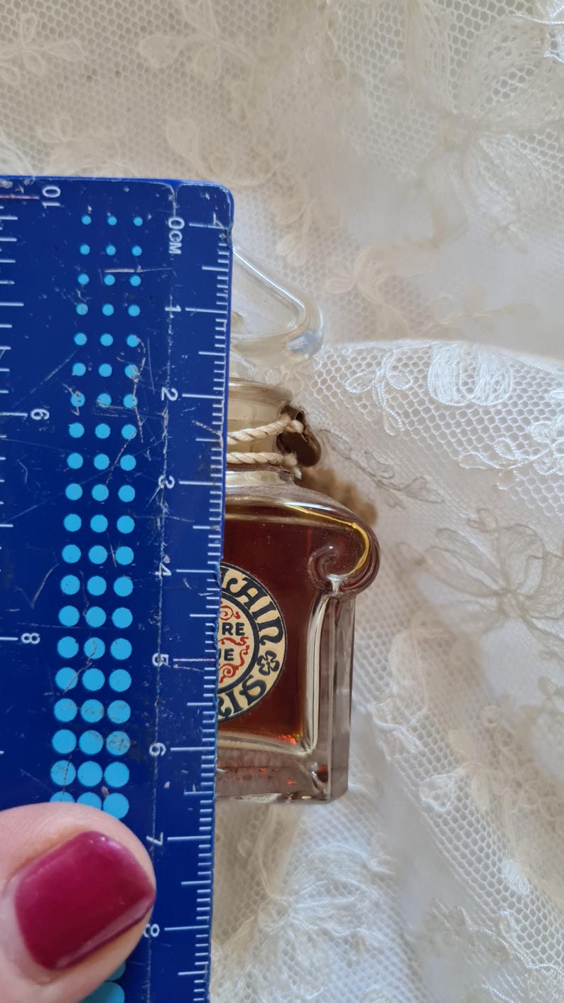 May include: A small glass bottle with a brown liquid inside. The bottle has a gold-colored label with the text "Irish Mist" and a shamrock design. The bottle is about 5 cm tall.