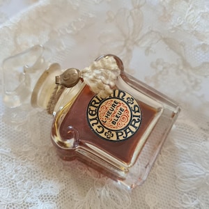 May include: A vintage glass bottle of perfume with a clear glass stopper and a label that reads "Guerlain L'Heure Bleue Paris".