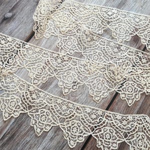 Può includere: Diverse strisce di pizzo color crema con bordo smerlato e intricati motivi floreali. Il pizzo è disposto su una superficie di legno invecchiato, evidenziando il suo design e la sua consistenza delicati. Ideale per cucito e progetti artigianali.