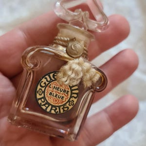 May include: A small, clear glass bottle of perfume with a gold-colored cap and a label that reads "Guerlain L'Heure Bleue Paris".