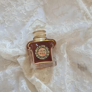 May include: A small, clear glass bottle of perfume with a gold cap and label. The label reads "L'Heure Bleue Paris".