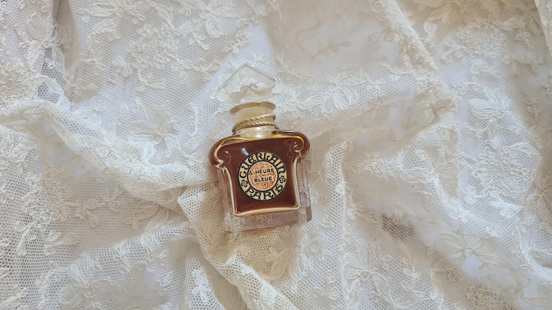 May include: A small, clear glass bottle of perfume with a gold cap and label. The label reads "L'Heure Bleue Paris".