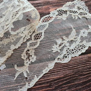 Puede incluir: Un delicado encaje blanco con un patrón floral. El encaje está sobre una superficie de madera marrón.
