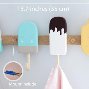 May include: A wooden wall-mounted coat rack featuring four colorful popsicle-shaped hooks. The rack is 13.7 inches (35 cm) wide and includes mounting hardware. The hooks are painted in pastel colors with decorative details.