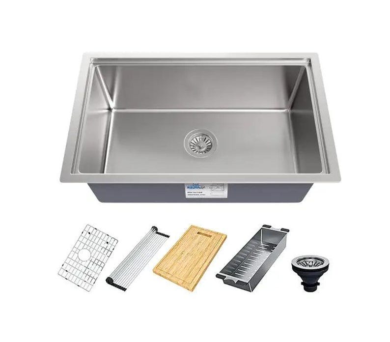 Puede incluir: Un fregadero de cocina de acero inoxidable con un solo cuenco y un desag&uuml;e en el centro. El fregadero est&aacute; rodeado por una encimera blanca e incluye una variedad de accesorios, como una tabla de cortar, un escurridor, un escurridor de platos y un colador.