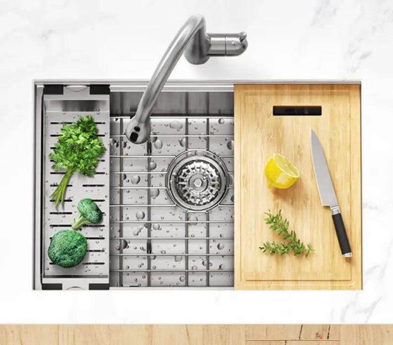 Puede incluir: Un fregadero de cocina de acero inoxidable con una tabla de cortar integrada y un grifo extra&iacute;ble. El fregadero tiene un desag&uuml;e de rejilla y est&aacute; lleno de agua. Hay verduras y un lim&oacute;n en la tabla de cortar.