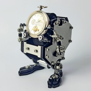 Op de afbeelding: Een unieke steampunk-stijl klok in de vorm van een robot. De klok heeft een ronde, goudkleurige wijzerplaat met ingewikkelde details, geplaatst in een zwart en zilverkleurig metalen lichaam. De robot heeft beweegbare armen en benen en staat op een witte ondergrond.
